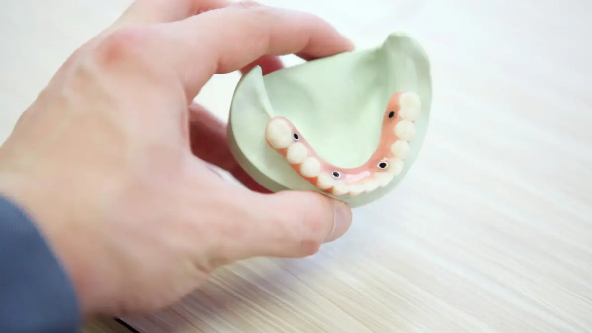 A hand holding a dental model of a lower denture